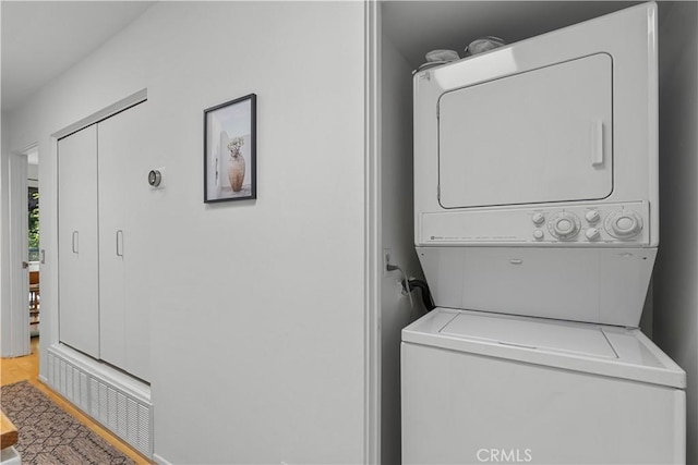 clothes washing area with visible vents, laundry area, stacked washer / drying machine, and wood finished floors