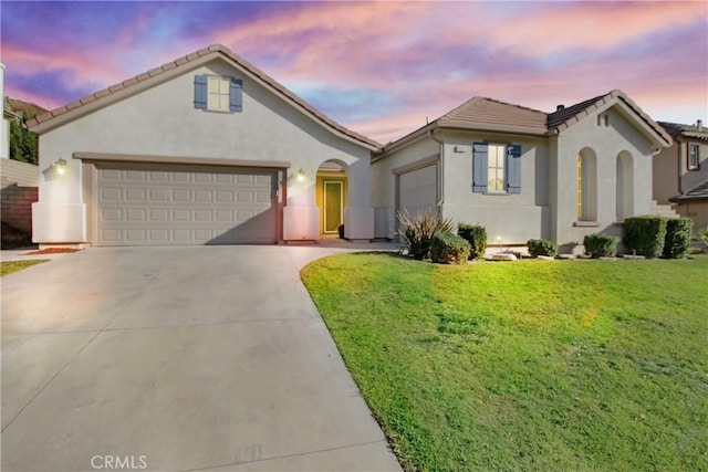 mediterranean / spanish home featuring stucco siding, an attached garage, driveway, and a yard