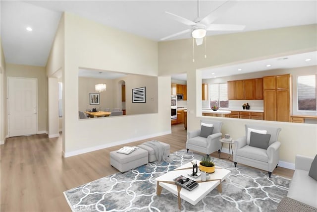 living room with light wood finished floors, arched walkways, a ceiling fan, and baseboards