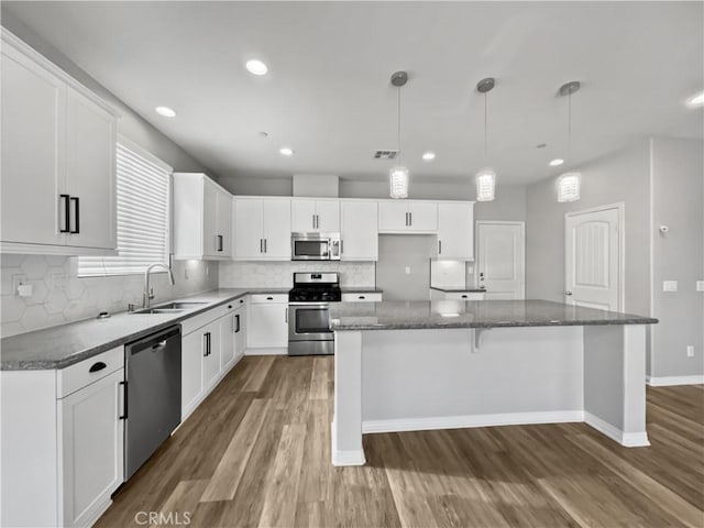 kitchen with a sink, a center island, appliances with stainless steel finishes, decorative backsplash, and dark wood-style flooring