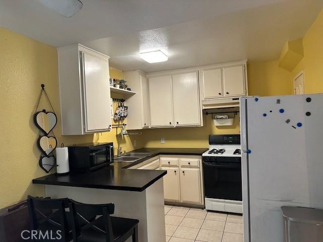 kitchen featuring a peninsula, freestanding refrigerator, black microwave, range with gas cooktop, and dark countertops