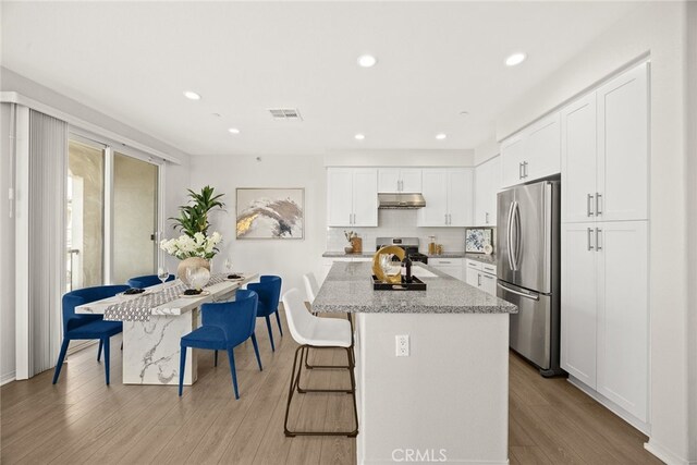 kitchen with visible vents, a breakfast bar, light wood-style floors, under cabinet range hood, and appliances with stainless steel finishes