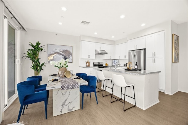 kitchen with visible vents, a kitchen island with sink, under cabinet range hood, appliances with stainless steel finishes, and a kitchen bar