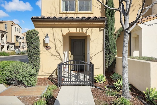 view of exterior entry featuring a tiled roof, a gate, and stucco siding