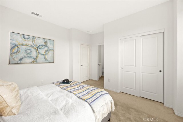 bedroom with a closet, visible vents, and light colored carpet