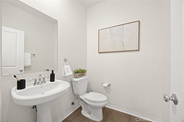 half bath with baseboards, toilet, and wood finished floors