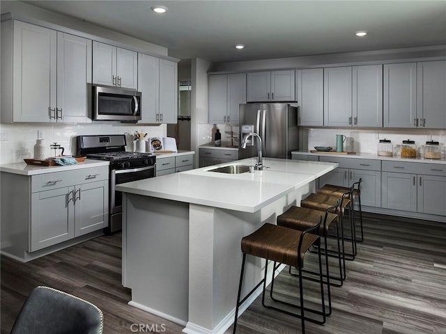 kitchen featuring gray cabinetry, a sink, a kitchen breakfast bar, stainless steel appliances, and light countertops