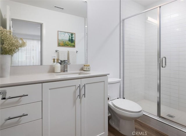 bathroom featuring visible vents, toilet, a stall shower, wood finished floors, and vanity