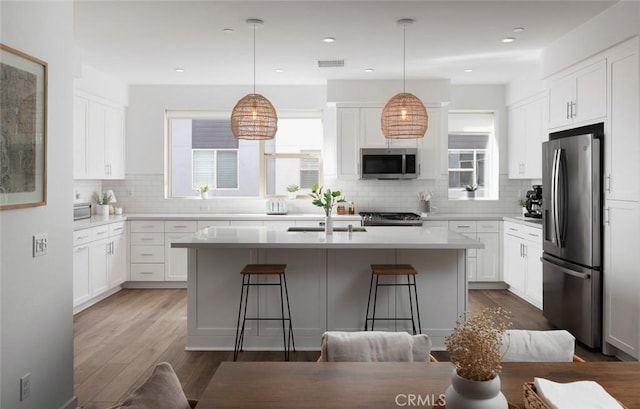 kitchen featuring visible vents, dark wood-type flooring, a center island with sink, white cabinetry, and appliances with stainless steel finishes