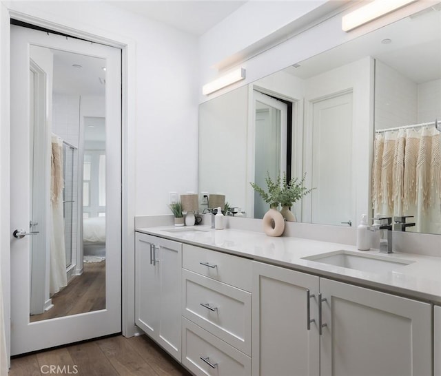 ensuite bathroom featuring a sink, ensuite bath, wood finished floors, and double vanity