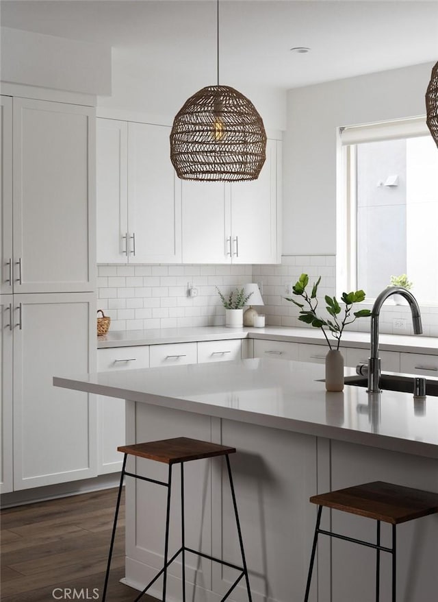 kitchen with a kitchen bar, a sink, white cabinets, light countertops, and dark wood-style flooring