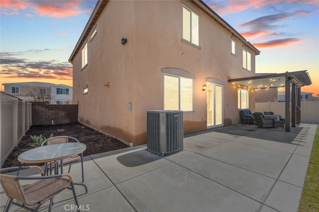 back of house at dusk with stucco siding, central air condition unit, a fenced backyard, and a patio area