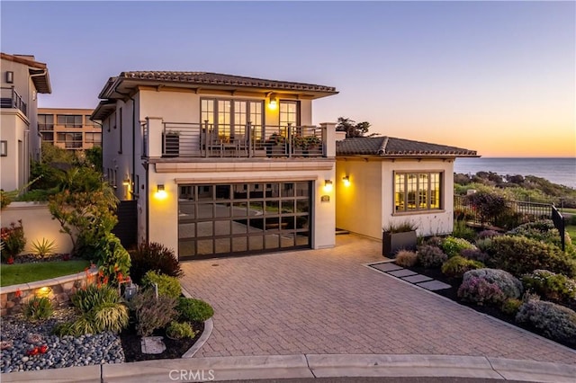 mediterranean / spanish-style house with a water view, a tile roof, stucco siding, decorative driveway, and a balcony