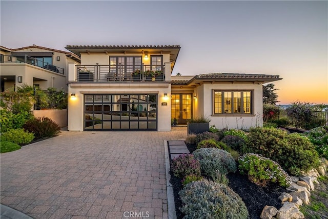 mediterranean / spanish-style house featuring stucco siding, decorative driveway, french doors, a balcony, and a tiled roof