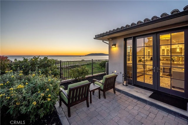 patio terrace at dusk featuring french doors, a water view, and fence