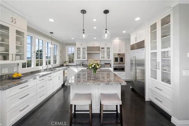 kitchen featuring a sink, under cabinet range hood, a kitchen island, white cabinetry, and stainless steel appliances