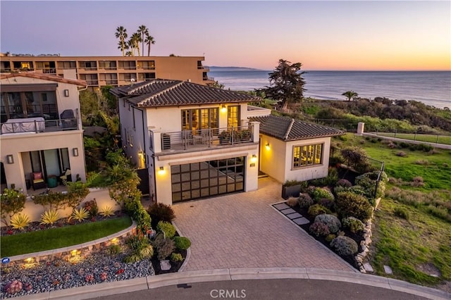 view of front of home featuring decorative driveway, a water view, a balcony, and stucco siding