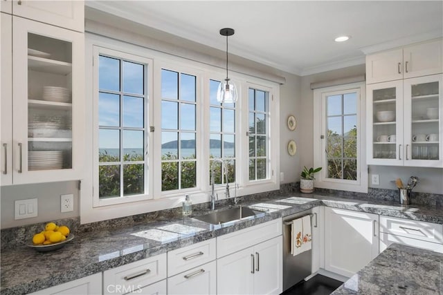 kitchen featuring pendant lighting, ornamental molding, white cabinetry, dark stone counters, and glass insert cabinets