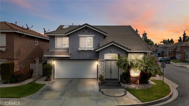 traditional home with stucco siding, stone siding, concrete driveway, an attached garage, and a tiled roof