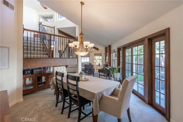 carpeted dining space with visible vents, baseboards, a chandelier, stairs, and vaulted ceiling