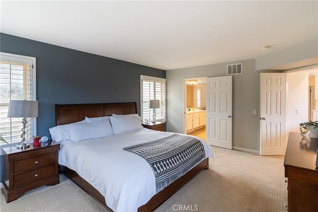 bedroom featuring baseboards, visible vents, ensuite bathroom, and light carpet