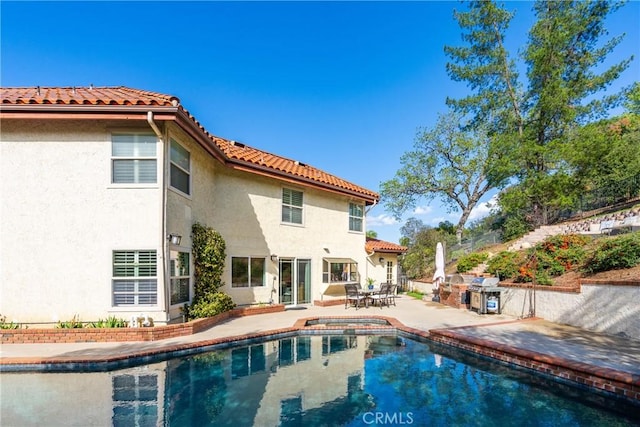 rear view of property featuring stucco siding, a pool with connected hot tub, a patio, an outdoor kitchen, and a tiled roof