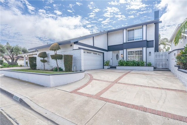 view of front of property with stucco siding, driveway, an attached garage, and a gate