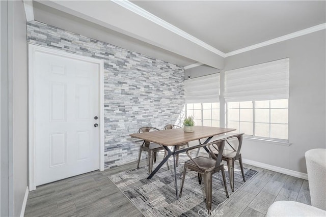 dining room featuring an accent wall, crown molding, wood finished floors, and baseboards