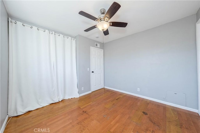 empty room with visible vents, light wood-style flooring, a ceiling fan, and baseboards