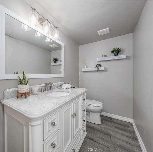 half bath with visible vents, toilet, wood finished floors, baseboards, and vanity