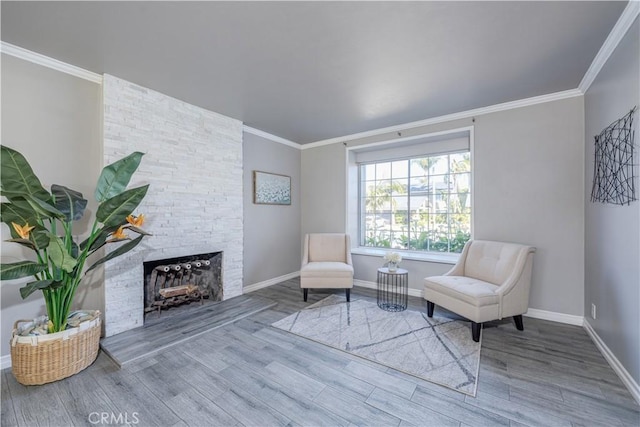 living area with a stone fireplace, crown molding, wood finished floors, and baseboards