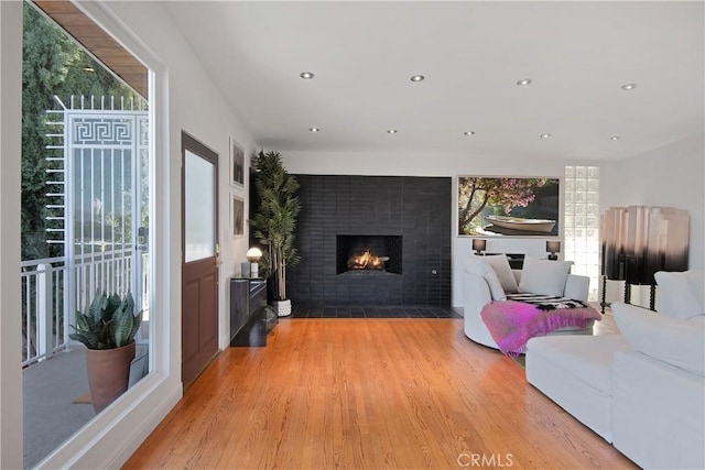 living room with recessed lighting, a lit fireplace, and wood finished floors