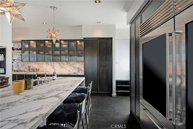 kitchen with a breakfast bar, stainless steel built in refrigerator, glass insert cabinets, recessed lighting, and decorative backsplash