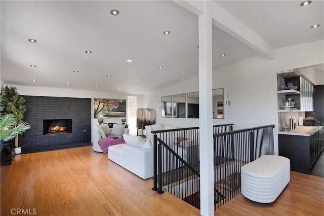 living room with recessed lighting, a fireplace with flush hearth, light wood-style floors, and vaulted ceiling with beams