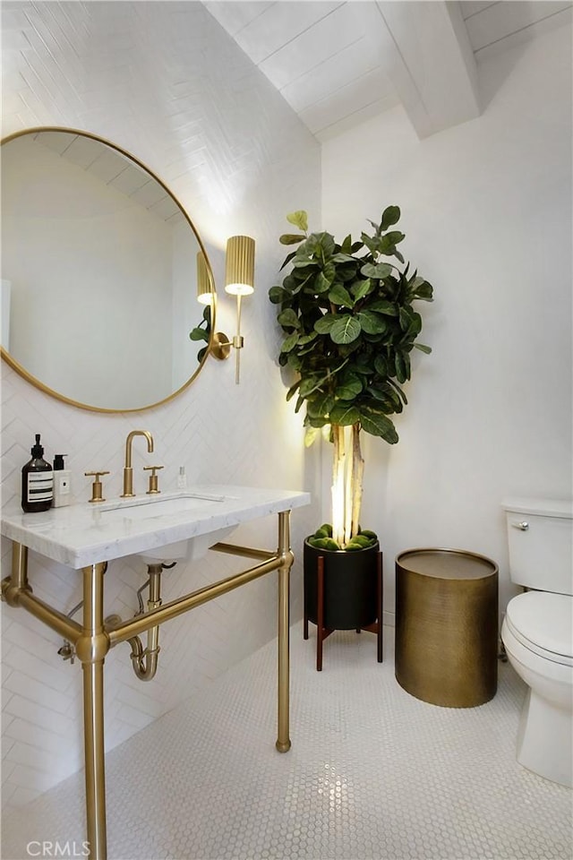 half bathroom featuring tile patterned floors, beamed ceiling, and toilet