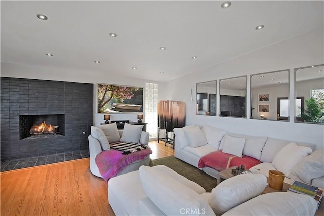 living room featuring vaulted ceiling, a fireplace with flush hearth, recessed lighting, and wood finished floors