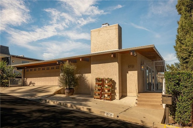 view of front facade featuring concrete driveway, a chimney, a garage, and stucco siding