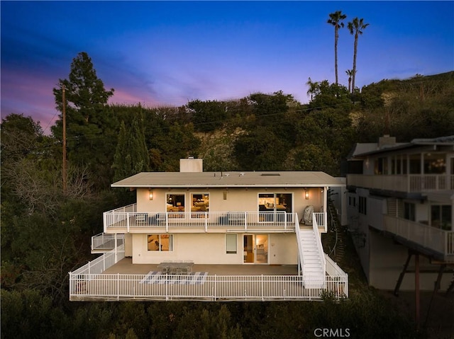 rear view of house with a patio, a balcony, stucco siding, and a chimney