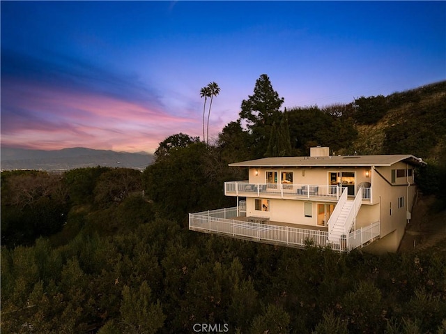 back of property with a balcony, a forest view, a chimney, and stucco siding