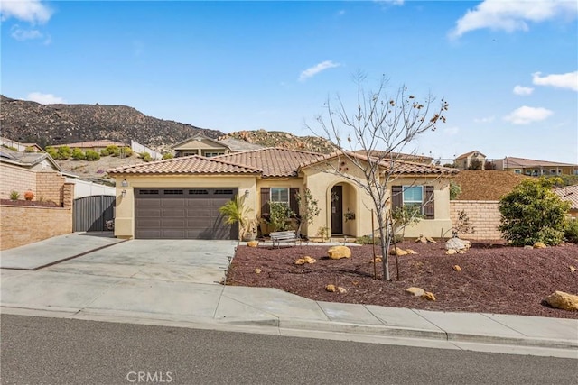 mediterranean / spanish house featuring a tiled roof, stucco siding, an attached garage, and a gate