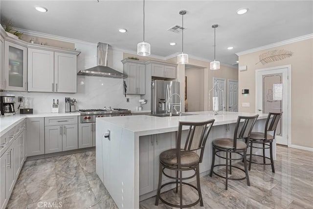 kitchen with visible vents, gray cabinetry, wall chimney range hood, appliances with stainless steel finishes, and a sink