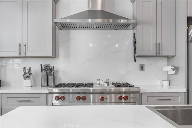 kitchen featuring stove, gray cabinets, wall chimney range hood, and backsplash