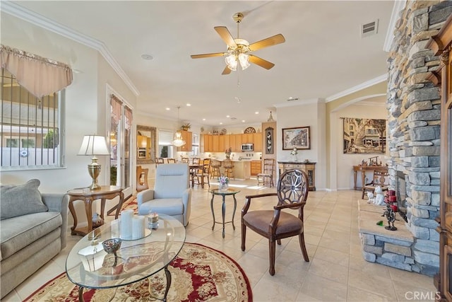 living room with visible vents, a ceiling fan, arched walkways, crown molding, and light tile patterned floors