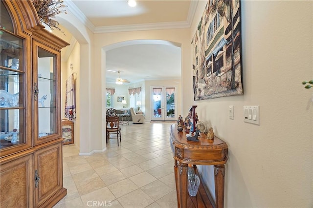 corridor featuring arched walkways, light tile patterned floors, crown molding, and baseboards