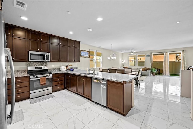 kitchen with light stone countertops, a peninsula, marble finish floor, stainless steel appliances, and a sink