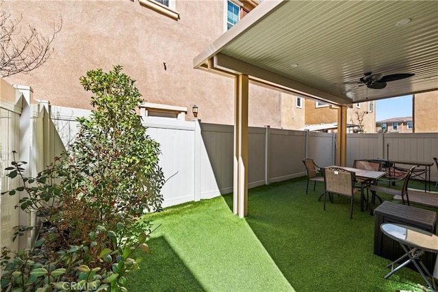 view of yard featuring ceiling fan, a fenced backyard, and outdoor dining space