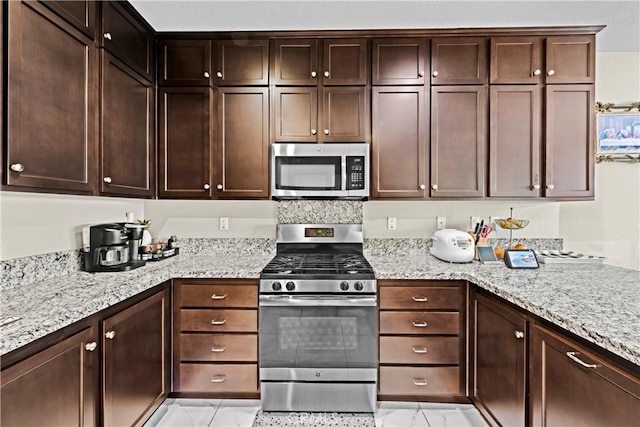 kitchen featuring dark brown cabinets, marble finish floor, appliances with stainless steel finishes, and light stone countertops