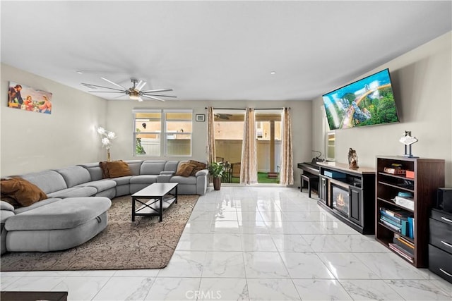 living room featuring a glass covered fireplace, a ceiling fan, and marble finish floor