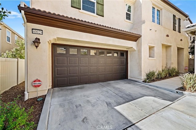 exterior space featuring an attached garage, fence, driveway, and stucco siding