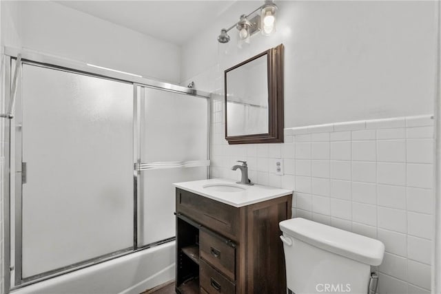 full bathroom with vanity, tile walls, toilet, and combined bath / shower with glass door